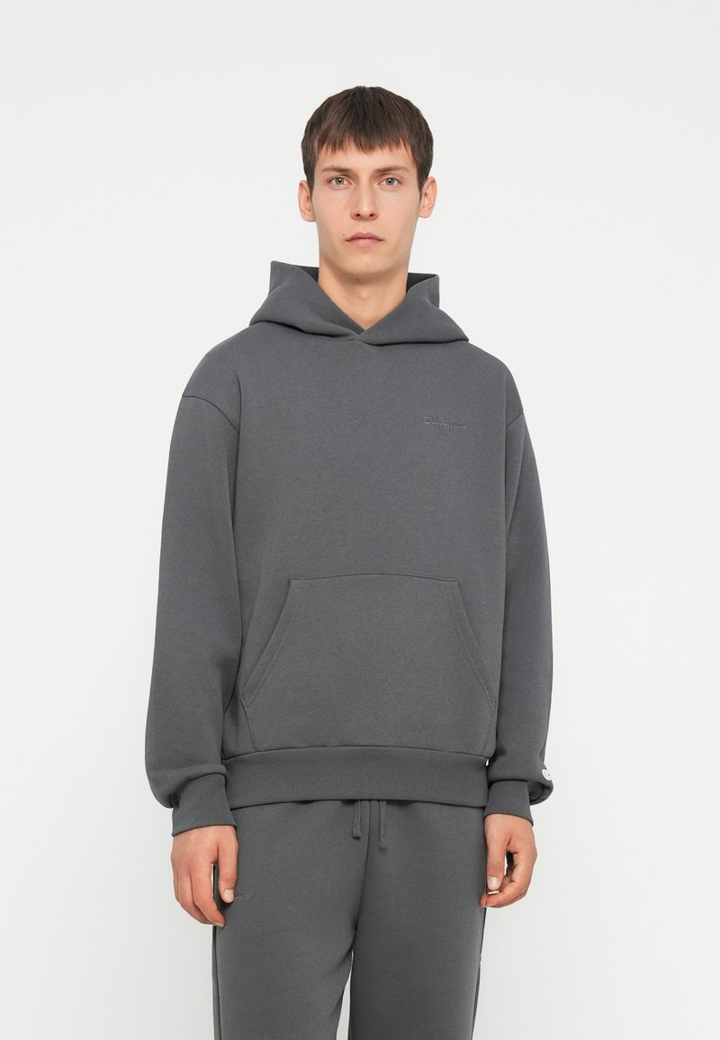 Sudadera gris de tejido suave, con bolsillo canguro, puños y dobladillo acanalados, y un logo sutil en el pecho. Combínala con pantalones de chándal a juego.