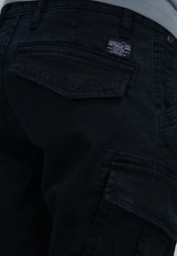 Donkerblauwe cargobroek van duurzaam materiaal, voorzien van meerdere zakken, een logo-label en een gestructureerde afwerking.