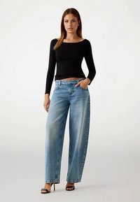 Sort langærmet top kombineret med løse lyseblå jeans i denim. Jeansene har en falmet vask og traditionel femlomme-stil.