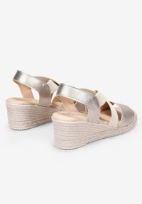 Sandalias de cuña con un acabado metálico dorado, que cuentan con tiras elásticas y una suela texturada similar al corcho, ideales para un uso casual.