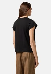 Schwarzes, kurzärmeliges, locker sitzendes Oberteil mit rundem Ausschnitt. Weicher Stoff, minimalistisches Design, kombiniert mit braun gestreiften, hochtaillierten Hosen.