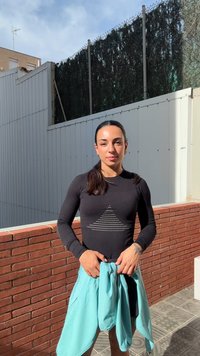 Svart långärmad topp med ett triangulärt mönster, i kombination med ljusblå shorts. Synlig tegelvägg och texturerade plattor i bakgrunden.