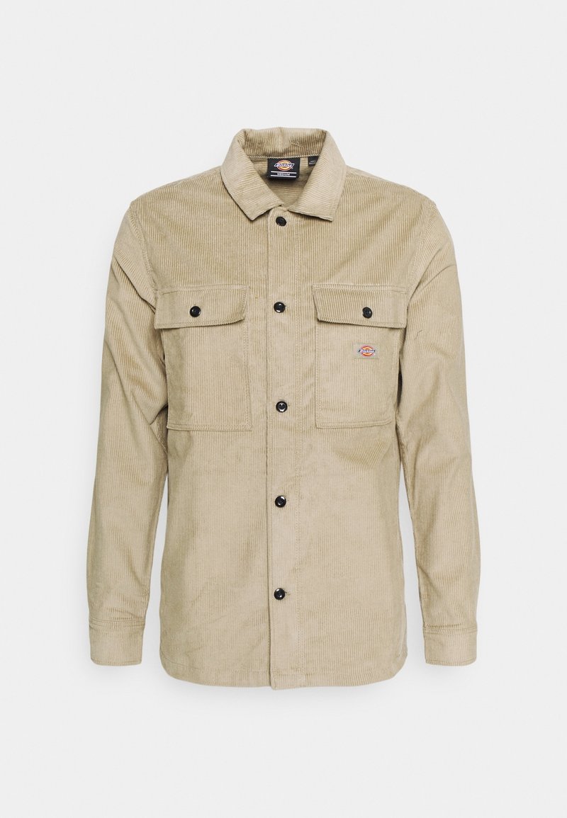 Camicia giacca in corduroy beige con maniche lunghe, chiusura con bottoni davanti, due tasche sul petto e una piccola toppa con logo sul lato sinistro.