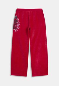 Červené tepláky s širokými nohavicami z mäkkej látky, so štruktúrovaným dizajnom a čiernymi grafickými akcentmi na jednej strane.