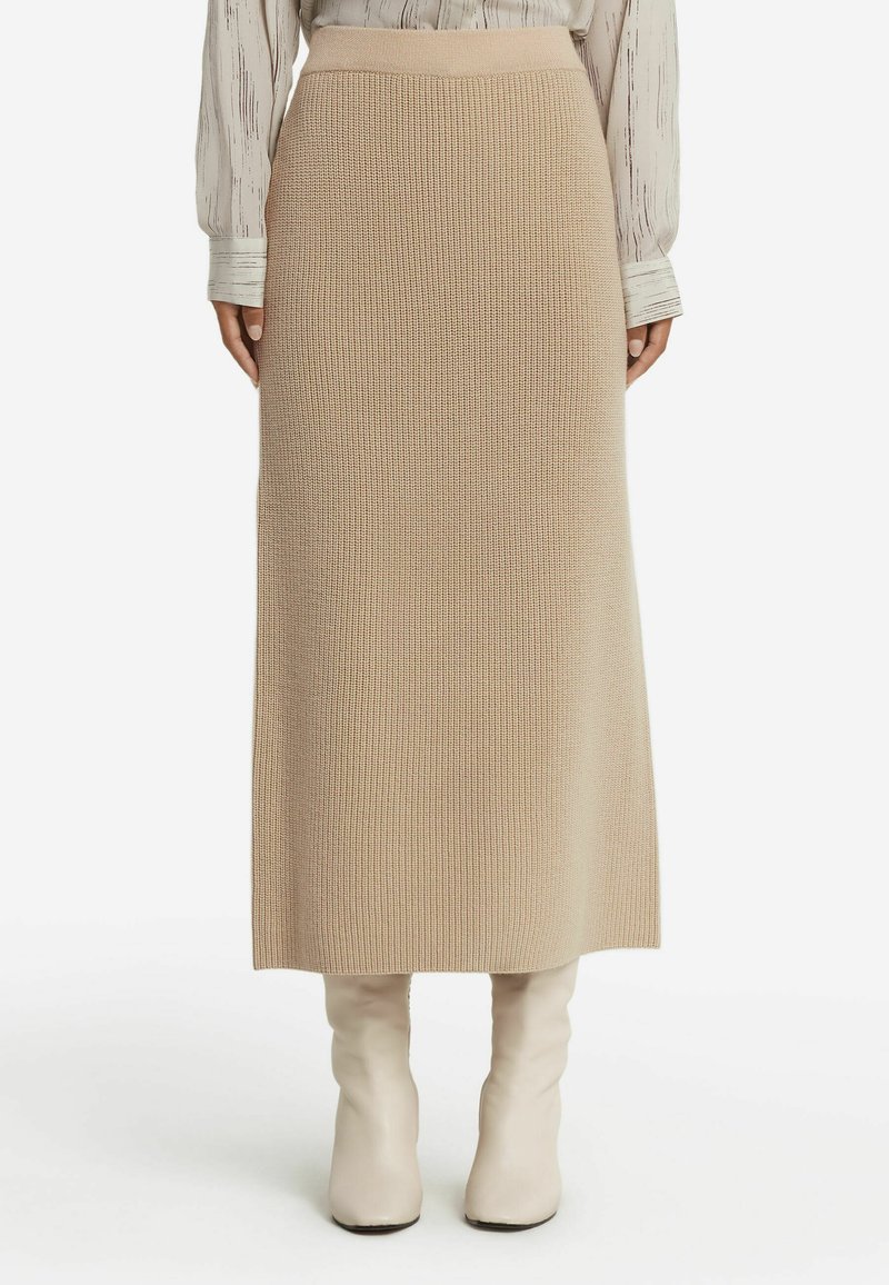 Stickad beige maxikjol med ribbad textur, med hög midja. Kombineras med beige knähöga stövlar, vilket fulländar den neutrala färgpaletten.