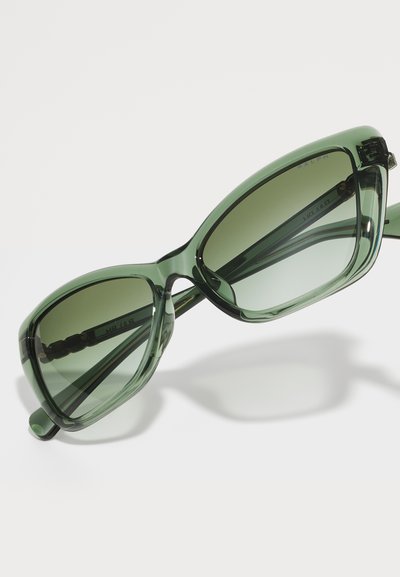 Occhiali da sole verdi oversize con montatura in plastica lucida e lenti verde scuro sfumate. Caratterizzati dalla loro forma unica e audace e dalla consistenza liscia.