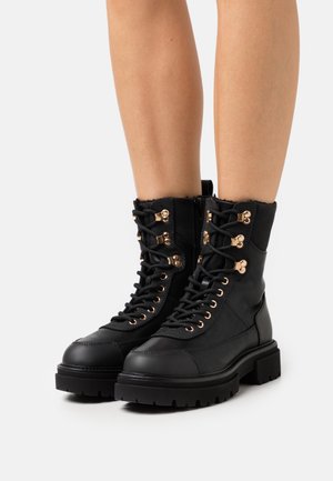 Botas de cuero negro hasta el tobillo con punta redonda, acentos en dorado, cordones en la parte delantera y un cuello texturizado, que cuentan con una suela robusta.