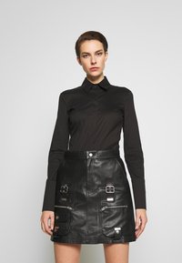 Black button-up shirt with long sleeves paired with a high-waisted black leather skirt featuring pockets and metallic hardware accents.