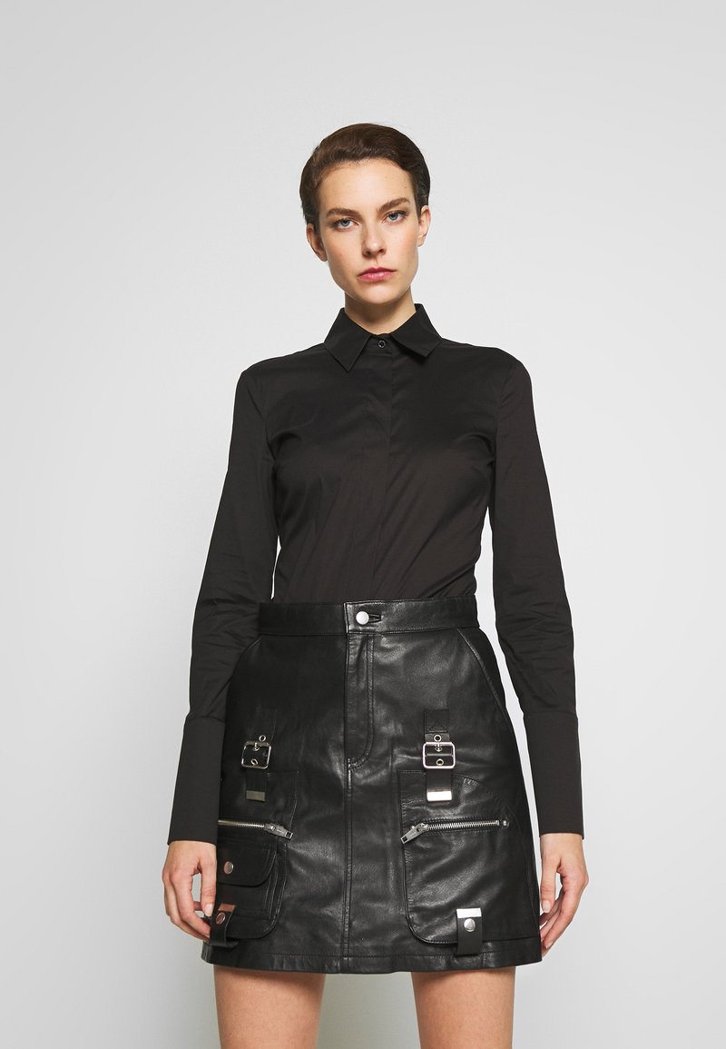 Black button-up shirt with long sleeves paired with a high-waisted black leather skirt featuring pockets and metallic hardware accents.