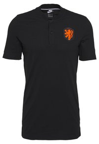 Musta lyhythihainen polo-paita, jossa on kaksi nappia, Nike-logo kauluksessa ja oranssi leijonasymboli vasemmassa rinnassa.
