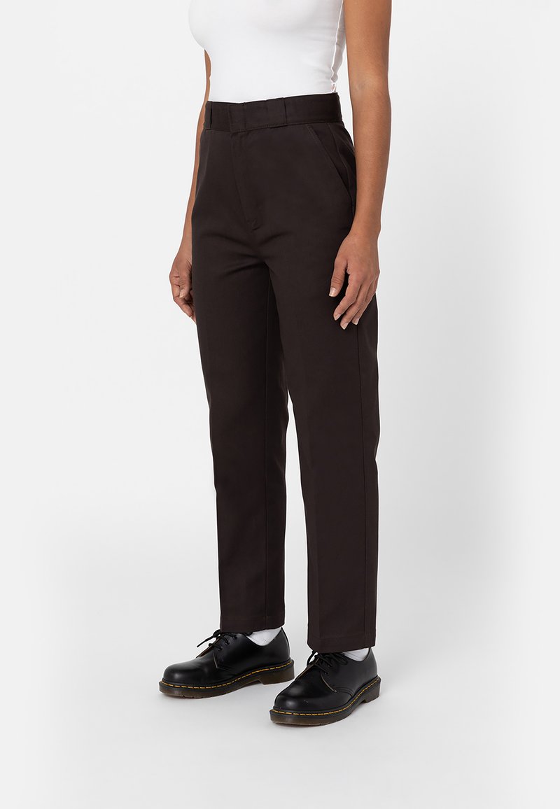 Pantalones marrones de talle alto con un corte recto, que cuentan con bolsillos laterales y una tela suave. Combinados con zapatos negros con cordones y calcetines blancos.