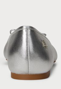 Srebrne metaliczne baleriny o gładkiej teksturze, okrągłym czubku i małym logo marki na pięcie. Brązowa gumowa podeszwa z detalami w postaci sznurków.