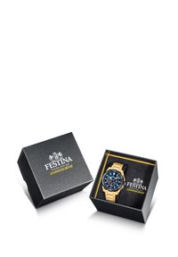 Montre dorée avec un cadran bleu, bracelet noir et plusieurs sous-cadrans, présentée dans une boîte cadeau noire texturée avec des accents jaunes.