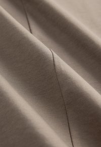 Tessuto marrone con una texture liscia, caratterizzato da una sottile lucentezza e cuciture visibili. Il materiale appare morbido e leggermente drappeggiato.