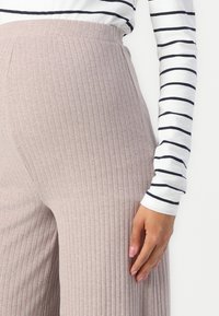 Hellrosa gerippte Strickhose mit hoher Taille, die vertikale Streifen und einen bequemen Sitz aufweist. Kombination mit einem dünn gestreiften Langarmoberteil.