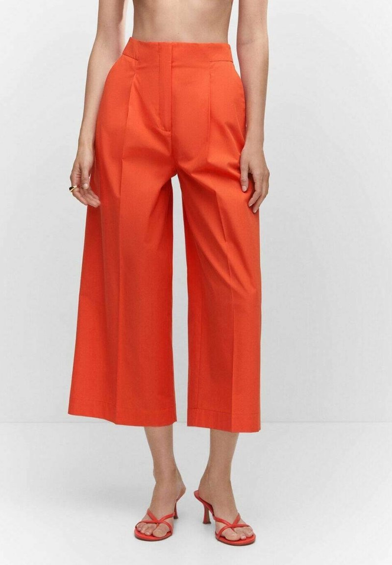 Pantalon orange court taille haute à jambes larges, associé à des sandales à talons à brides assorties, sur une personne debout.