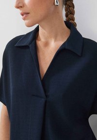 Chemise à col marine à manches courtes, en tissu texturé. Elle présente un décolleté en V profond et un léger plissage à l'avant.