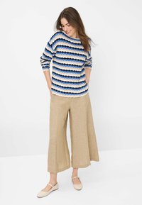 Gestreifter Strickpullover in Blau, Creme und Marineblau; breite beiger Leinenhose; helle Schuhe. Strukturiert mit gewellten Kanten.