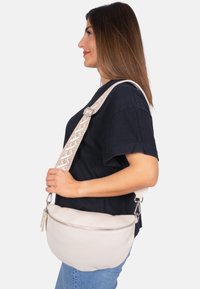 Weiße Leder-Umhängetasche mit strukturiertem Finish, ausgestattet mit einem dekorativen, gemusterten Riemen und einem Reißverschlussfach an der Vorderseite.