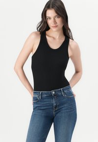 Svart ribbet bodysuit med brede skulderstropper, parret med blå høytlivde skinny jeans med klassisk fem-lommers design.
