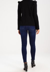 Czarny sweter z falbaniastymi akcentami na ramionach, zestawiony z ciemnoniebieskimi rurkami i botkami za kostkę. Gładka tekstura i dopasowany fason.