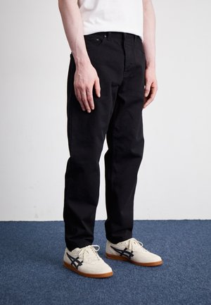 Schwarze Jeans mit geradem Schnitt, ausgestattet mit fünf Taschen und einem klassischen Knopfverschluss. Tragen mit hellen, strukturierten Sneakern.