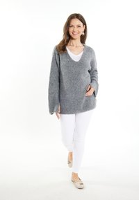 Pulover gri, tricotat, cu decolteu în V și mâneci lungi, asociat cu pantaloni albi și pantofi cu talpă joasă de culoare deschisă. Textură moale, croială lejeră.