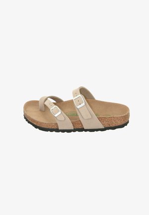 Beige suede sandal with two adjustable straps featuring silver buckles. Cork footbed and textured black rubber sole. Flat design.