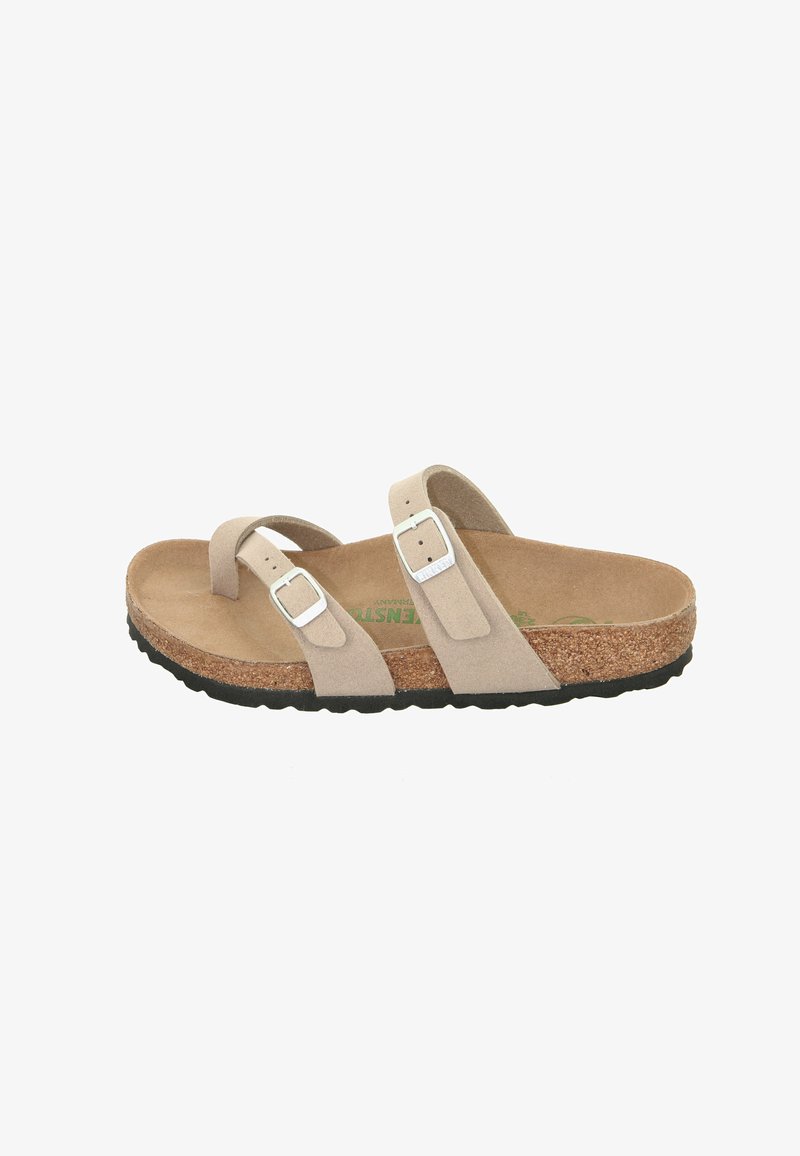 Beige suede sandal with two adjustable straps featuring silver buckles. Cork footbed and textured black rubber sole. Flat design.