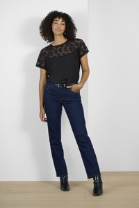Black top with lace detailing, short sleeves, and a round neckline, paired with dark blue denim jeans. Black ankle boots complete the look.