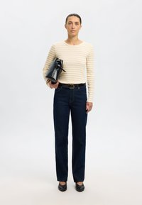 Camisola de mangas compridas às riscas em creme e bege, jeans de ganga escura de cintura subida, cinto preto, mala preta com detalhe de laço, sapatilhas pretas.