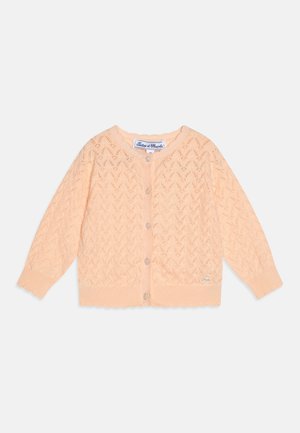 Ferskenfarvet strikket cardigan med zigzag-mønster, rund halsudskæring, knaplukning foran og bølget kant med et lille logo-mærke nederst til venstre.