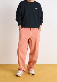 Marinblå college-tröja med rund halsringning och vitt tryck, tillsammans med ljusrosa, löst sittande byxor och vita sneakers med grå och röda detaljer.