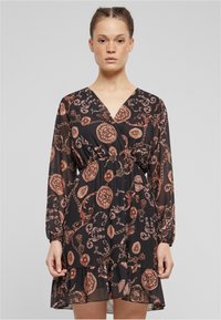 Rochie neagră transparentă cu mâneci lungi, decolteu în V și talie elastică. Prezintă un lanț bronzit și modele florale, finisată cu o margine volan.
