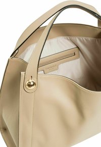 Borsa beige con un'esterno in pelle leggermente texturizzato, manico superiore singolo, accessori in oro e interni a strisce con una tasca con zip.