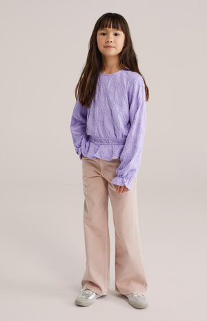 Haut à manches longues texturé lavande, taille superposée, associé à un pantalon ample rose clair et des baskets argentées, avec un design simple.