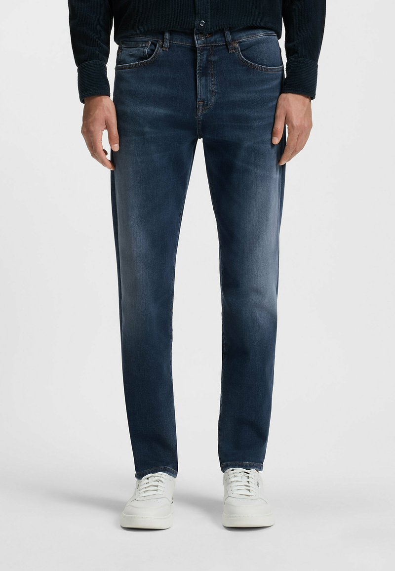 Donkerblauwe denim jeans met een slim fit, met voorzakken, subtiele vervaging en stiksels als accent. Gepaard met witte sneakers.