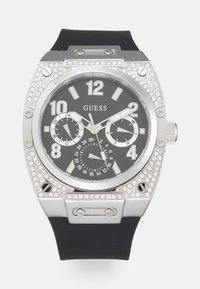 Reloj de acero inoxidable plateado con una correa de goma negra. Presenta un marcador negro, marcadores de hora blancos, tres subesferas y acentos de cristal.