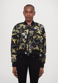 Black bomber jacket with intricate gold and white floral patterns, ribbed cuffs and hem, front zipper, and a contrasting pink collar.