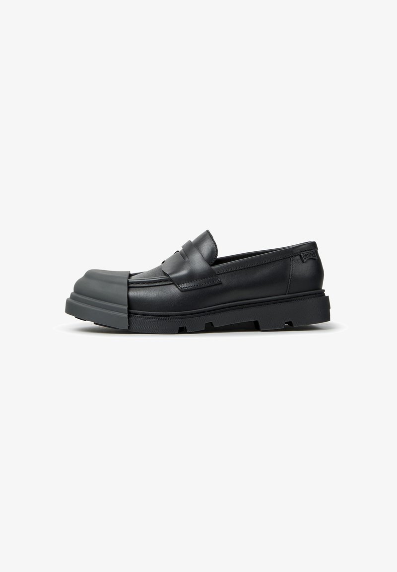 Mocassin en cuir noir avec une semelle en caoutchouc épaisse à nervures et un embout protecteur prolongé, vu de l'extérieur sur fond blanc.