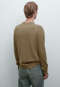 Brun stickad tröja med rund halsringning, ribbade ärmslut och fåll, i kombination med ljusgrå jeans. Mjuk textur, enkel design och avslappnad passform.