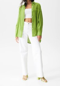 Chemise en lin vert clair à boutons avec une poche poitrine, associée à un jean blanc à jambe large et des sandales à talons vert clair.