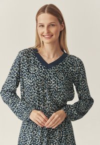 Bluză bleumarin cu decolteu în V, mâneci lungi și un model texturat de puncte albastre deschise și crem pe un fundal închis.