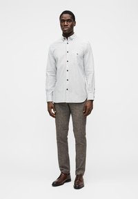 Cămașă cu dungi, butoniere, albă și bleumarin, croială ajustată, mâneci lungi. Asortată cu pantaloni maro texturati și pantofi maro eleganți.