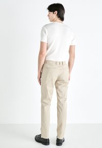 Beige bomullsbukser med rett fit, kombinert med en hvit ribbet t-skjorte med kort erme. Svarte sko fullfører antrekket.