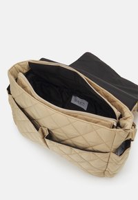 Borsa beige trapuntata con tasca esterna e scomparti interni. Presenta una chiusura con zip e rivestimento nero. Texture morbida e imbottita.
