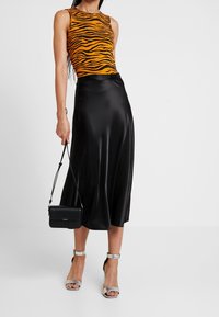 Tiger-Print orange ärmelloses Oberteil, schwarzer Satin-Midirock, silberne Riemchen-Heels und eine kleine schwarze Crossbody-Tasche. Glatte Texturen, taillierter Schnitt.
