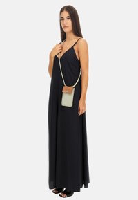 Abito lungo nero con spalline sottili, texture liscia e vestibilità comoda. Abbinato a una borsa a tracolla con un dettaglio marrone.