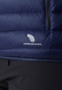 Marineblaues Steppweste mit horizontaler Naht, mit dem Etikett "Premium Daune", einem Logodetail und einem schwarzen Reißverschluss.