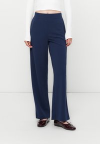 Marineblauwe wijde broek met een gladde, elastische tailleband. Bevat zijzakken en is gemaakt van een lichte, zachte stof. Gecombineerd met donkere schoenen.